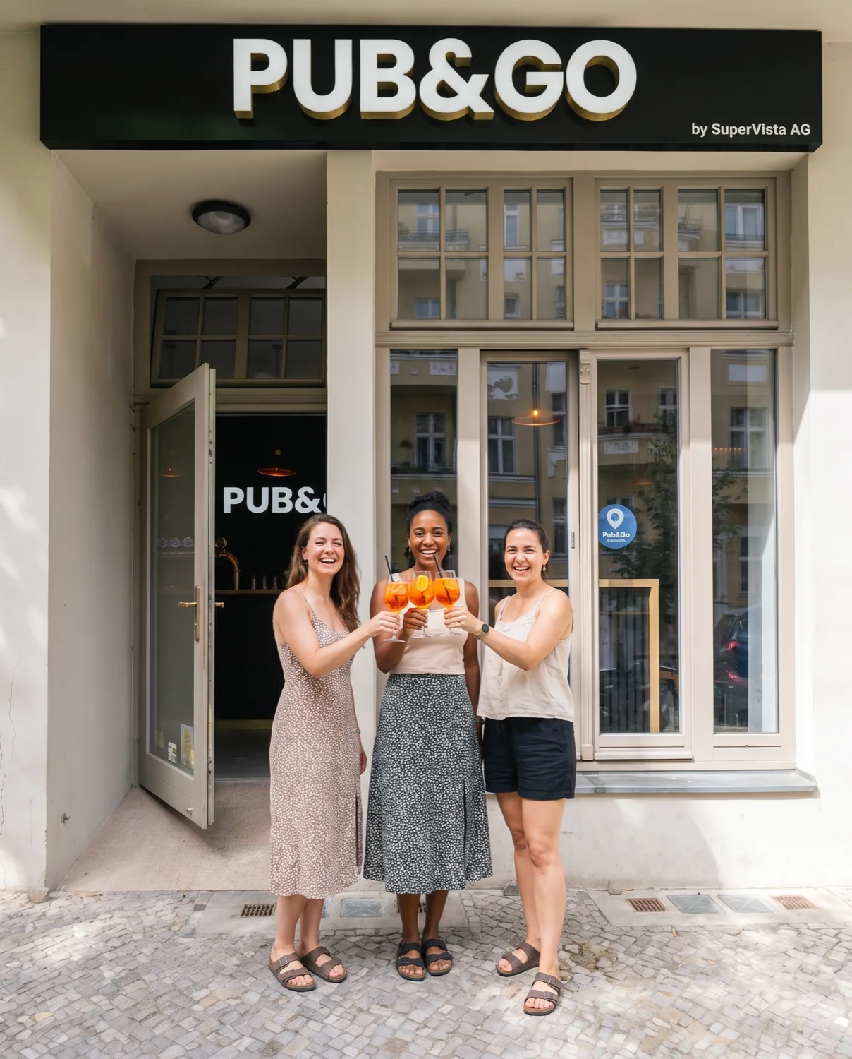 Drei Freundinnen stoßen mit Spritz vor dem Pub&Go Prenzlauer Berg an